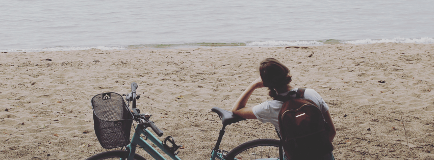 woman looks at water beside bicycle